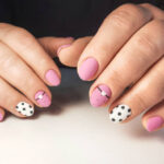 Round pink nails with black and white design. Women's hands with a delicate pink gel polish, with a design of a white heart and black stripes and spots.