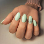 Gentle gel polish of pale turquoise color on almond-shaped nails with silver stripes. Nude manicure with shiny stripes design. Pastel color coating on the nails.