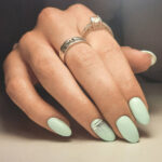 Gentle gel polish of pale turquoise color on almond-shaped nails with silver stripes. Nude manicure with shiny stripes design. Pastel color coating on the nails.