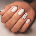 Women's hands with white gel polish and black French design. Women's manicure of milky delicate color with a spotted black design.